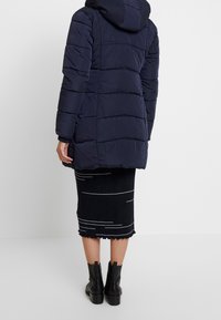 Padded navy coat with a hood, featuring horizontal stitching. Paired with a textured black skirt and black ankle boots. Simple design.