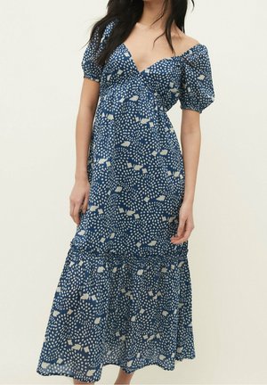 Blauwe midi-jurk met wit abstract stippenpatroon, pofkorte mouwen en een diepe V-hals gedragen door een staande persoon.