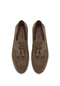 Mocasines de ante marrón con punta redonda, borlas decorativas y detalles de costura en contraste. Textura suave y diseño de fácil puesta.
