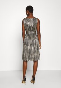 Robe mi-longue en tissu métallisé avec des rayures verticales, taille cintrée et jupe plissée. Portée avec des chaussures à talons hauts noires.