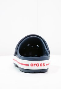 Crocs blu navy con retro chiuso, caratterizzati da fori di ventilazione e una suola bianca accentuata da dettagli rossi e il logo "crocs".