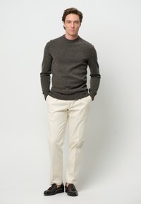 Grå stickad tröja, krämfärgade byxor och mörka skor. Tröjan har rundad hals och ribbade manschetter; byxorna är rakskurna med en slät textur.