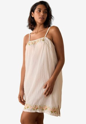 Lightweight, sheer cream dress with adjustable straps, embroidered floral accents, and textured dotted fabric, finishes just above the knee.