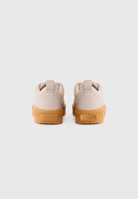 Et par beige sko med gummisåler, sett fra baksiden, med pull-tabs og "SOREL"-merke på hælen.