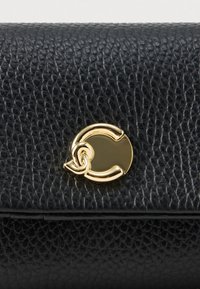 Zwart gestructureerd leren oppervlak met een kleine glanzende gouden ronde sluiting met in elkaar grijpende gebogen details.