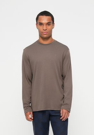 Chemise à manches longues marron en tissu doux avec un col rond. Présente un petit logo sur la poitrine et une coupe décontractée. Assortie à un pantalon à carreaux.