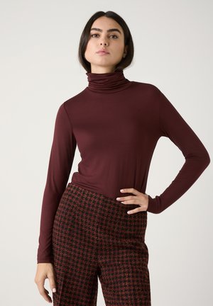 Bordeaux coltrui gemaakt van een gladde, elastische stof, gecombineerd met hoogzittende geruite broek in rood en zwart, met een ruitpatroon.