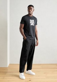 Svart bomull t-skjorte med hvitt grafisk trykk, kombinert med svarte bukser og hvite sneakers. Enkel design og avslappet passform.