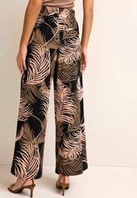 Wijde broek in zwarte stof met een roze en bruine palmbladerenpatroon. Elastische taille met geplooid detail; gladde, lichte textuur.