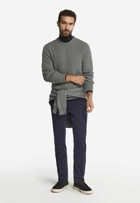 Grå ribbad tröja med rundad halsringning, kombinerad med marinblå byxor och mörka sneakers. Ljus struktur och lagerdesign synlig.