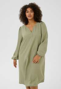 Robe longue à manches longues verte clair avec un décolleté en V, des poignets froncés et une coupe décontractée, fabriquée à partir d'un tissu texturé.