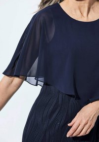 Marineblaues Zweiteiler-Kleid mit einer transparenten, fließenden oberen Schicht und einem strukturierten Unterteil, das horizontale Wellenmuster und einen subtilen Schimmer aufweist.