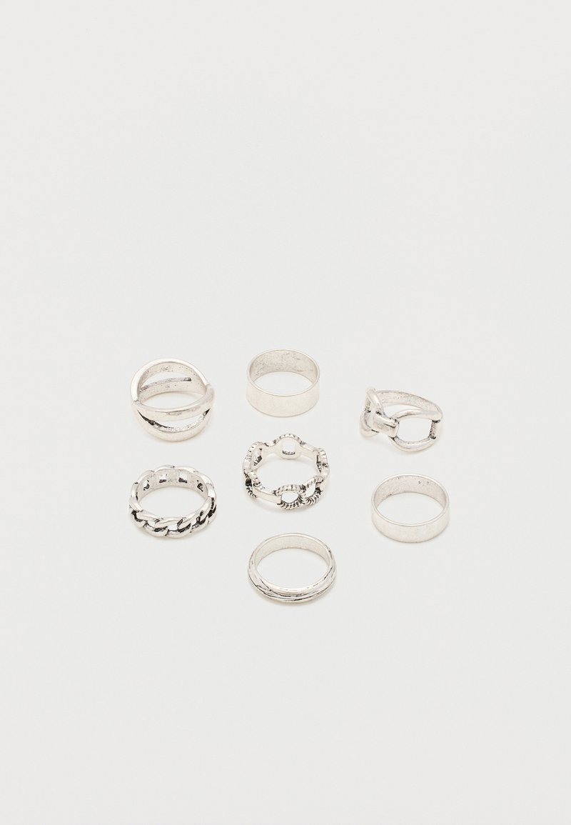 Επτά ασημένια δαχτυλίδια με διαφορετικά σχέδια, συμπεριλαμβανομένων απλών λωρίδων, αλυσιδωτών συνδέσμων και διακοσμητικών μοτίβων, τοποθετημένα σε λευκό φόντο.