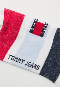 Multicolored sock with red, white, blue, and dark navy stripes; features "TOMMY JEANS" text and a logo patch for branding.