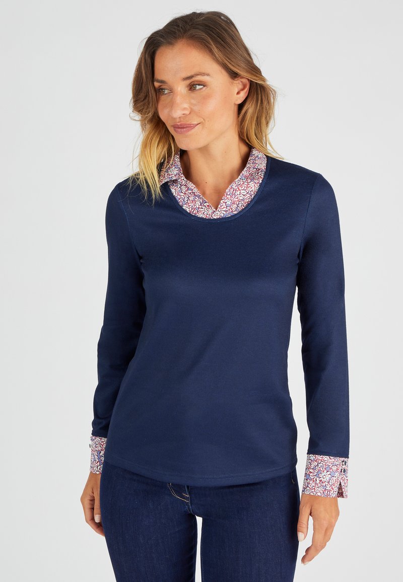 Haut à manches longues bleu marine avec un col et des poignets à imprimé floral. Tissu doux, conception ajustée, encolure arrondie et motifs contrastés.