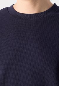 Granatowy sweter o fakturowanej strukturze z prążkowanym dekoltem, z subtelnym wzorem w wafle i miękkim, przewiewnym materiałem.