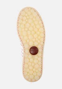Suela de un zapato con una superficie texturizada que presenta patrones circulares, color beige claro y un logotipo circular marrón en el centro.