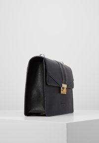 Borsa a tracolla in pelle nera con una forma strutturata, dotata di una chiusura in oro e un interno texture. Ha una parte superiore piatta e pannelli laterali.