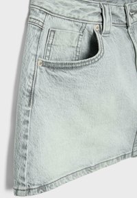 Jupe en denim bleu clair montrant une poche avant, des passants de ceinture et une texture de tissu délavé sur fond blanc.