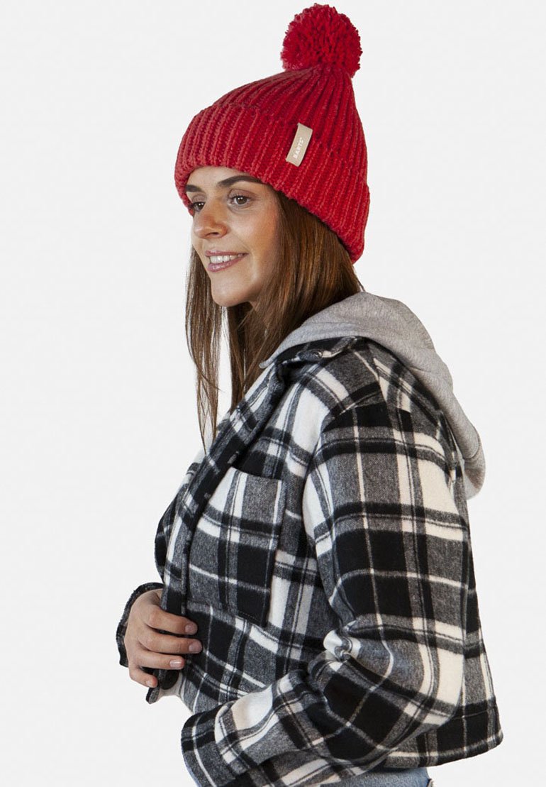Red knitted beanie with a pom-pom, paired with a black and white plaid flannel jacket featuring a hood and front pocket, layered over a gray hoodie.