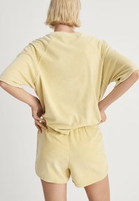 Geel fleece loungewear-set met een relaxed-fit, kortemouwen top en bijpassende shorts met een elastische tailleband. Zachte textuur overal.