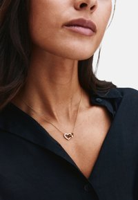 Artimos planas žmogaus, dėvinčio aukso grandinėlę su širdies formos pakabuku, išklotu mažais akmenėliais, ir paprastu aukso žiedo žavesiu.