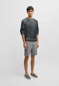 Tumma sininen neulepaita raidallisella tekstuurilla, yhdistettynä vaaleanharmaisiin sortseihin ja harmaisiin liukuvoittoisiin kenkiin. Yksinkertainen, moderni muotoilu.