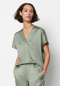 Top verde in satin con scollo a V e maniche corte, caratterizzato da una vestibilità rilassata e una texture morbida. Abbinato a pantaloni leggeri coordinati.
