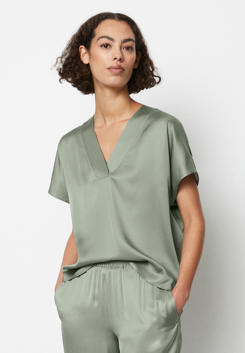 Top verde in satin con scollo a V e maniche corte, caratterizzato da una vestibilità rilassata e una texture morbida. Abbinato a pantaloni leggeri coordinati.