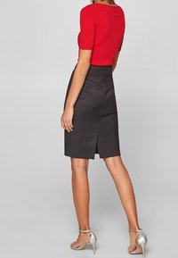 Rotes geripptes Kurzarmoberteil mit Knopfdetail auf der Rückseite, kombiniert mit einem schwarzen Bleistiftrock mit einem Schlitzausschnitt hinten. Silberne Riemchenheels.