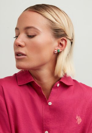 Orecchini a bottone in argento con una pietra rettangolare rosa e una pietra quadrata verde, indossati con una camicia rosa con colletto. Texture lisce, design minimale.