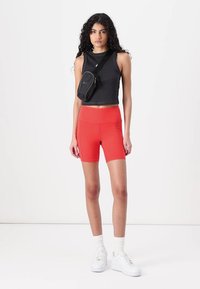 Black sleeveless crop top, red tight shorts, and white sneakers. Small black bag worn crossbody. Smooth materials and fitted design.