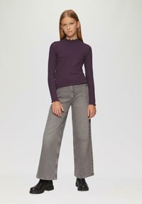 Paarse geribde lange mouw top met een geschulpte halslijn, gecombineerd met grijze denim jeans met wijde pijpen en zwarte robuuste enkellaarsjes.