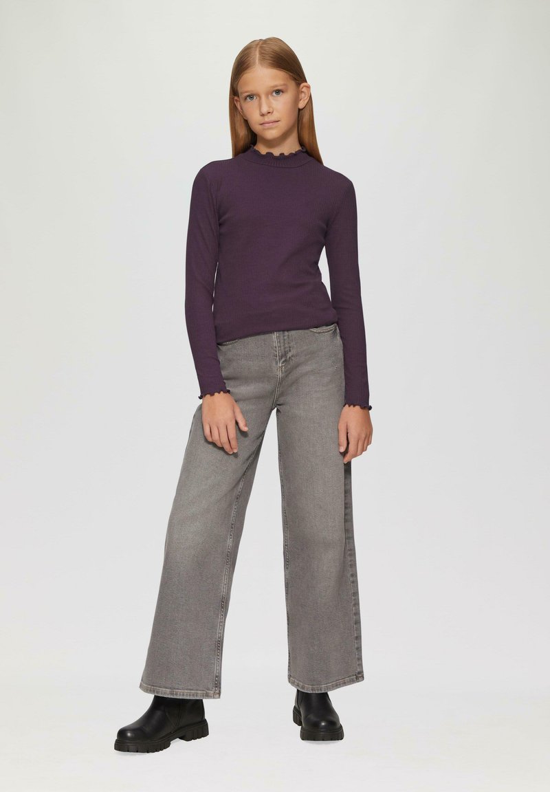 Paarse geribde lange mouw top met een geschulpte halslijn, gecombineerd met grijze denim jeans met wijde pijpen en zwarte robuuste enkellaarsjes.