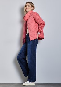 Ljusrosa quiltad jacka, krämfärgad tröja, mörkblå vida jeans och vita sneakers. Rosa scarf draperad runt nacken.