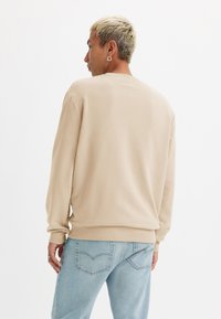 Beige sweatshirt met lange mouwen, ronde hals en een relaxte pasvorm. Gepaard met lichtblauwe jeans, toont minimale stitching en een casual ontwerp.