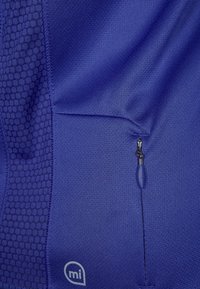 Violetti aktiivivaatteiden kangas, jossa on teksturoitu kuusikulmainen kuvio, sisäänrakennettu vetoketjullinen tasku ja pieni logo alakulmassa.