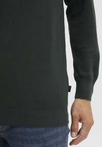 Pull verde închis, tricotat, cu textură cu nervuri, cu mansete și tiv ajustate. Prezintă o etichetă mică a brandului pe lateral. Design casual asortat cu blugi.