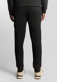 Schwarze Sweatpants aus weichem Stoff, mit schmal zulaufendem Bein und elastischem Bund. Kombiniert mit hellen Sportschuhen.