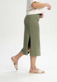 Olijfgroene midi-skirt met een zijsplit, gemaakt van zachte stof. Draag het met beige slide sandalen, wat een ontspannen en comfortabele uitstraling geeft.