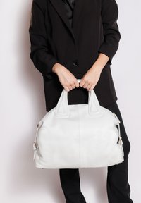 Borsa a mano in pelle bianca con forma arrotondata, manici superiori doppi e superficie testurizzata. Presenta accessori in tono oro e dettagli di cucitura visibili.