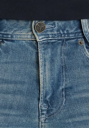 Jeans aus Denim mit einem hellblauen Waschung, kontrastierenden weißen Nähten und einem Metallknopfverschluss an der Taille. Nahaufnahme der Stofftextur.