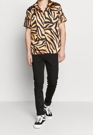 Camisa de manga corta en satén con un patrón de rayas de tigre en naranja y negro; diseño de botones en la parte delantera y cuello abierto, combinada con pantalones negros.