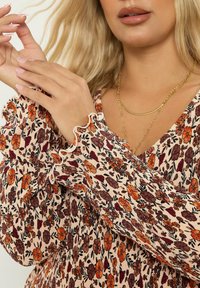 Blommig blus med en persikofärgad bakgrund och blommor i orange och brunt, volangkanter på ärmarna och en lös passform.