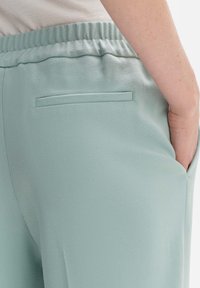 Pantaloni jogger verde chiaro realizzati in tessuto testurizzato con una vestibilità rilassata. Presentano un elastico in vita e una tasca sul retro.