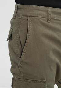 Cotton cargo shorts in olive green with side pockets, belt loops, and visible stitching. Fabric texture appears soft and durable.