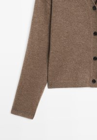 Bruine gebreide cardigan met een V-halsontwerp, lange mouwen en zwarte knopen. Zachte textuur en geribbelde zoomdetails.