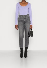 Długi rękaw, fioletowa bluzka z okrągłym dekoltem, szare dżinsy z wysokim stanem, czarne botki na obcasie i mała czarna torebka. Gładka tekstura w całym ubraniu.