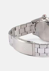 Rozsdamentes acél óra láncos karkötővel. Koptatott és polírozott felület, kör alakú tokkal és piros részlettel a koronán. A Timex embléma látható.