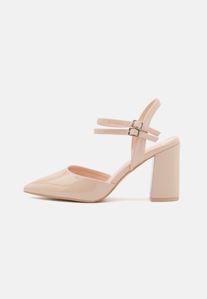 Zapato de charol rosa pálido con punta estrecha, dos correas en el tobillo con hebillas y tacón tipo bloque con un detalle metálico.